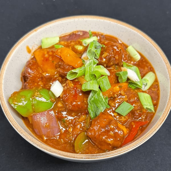 A bowl of Manchurian with bell peppers, onions, and scallions in a rich sauce.