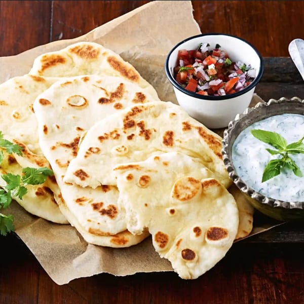 Freshly baked naan bread with cilantro, salsa, and a bowl of tzatziki sauce.