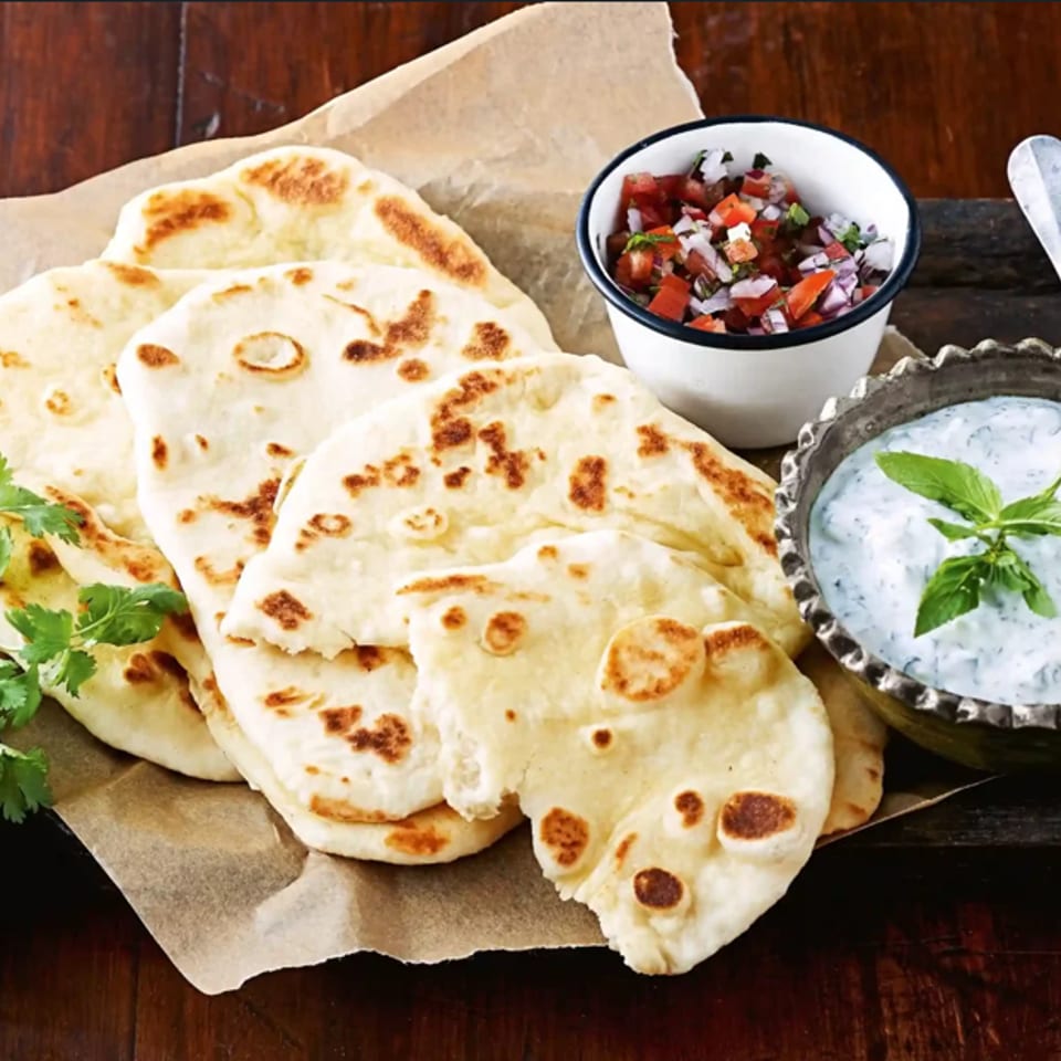 Freshly baked naan bread with cilantro, salsa, and a bowl of tzatziki sauce.