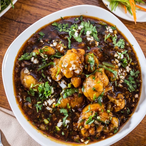 A white bowl filled with dark brown gravy, chicken pieces, and garnished with cilantro and chopped garlic.