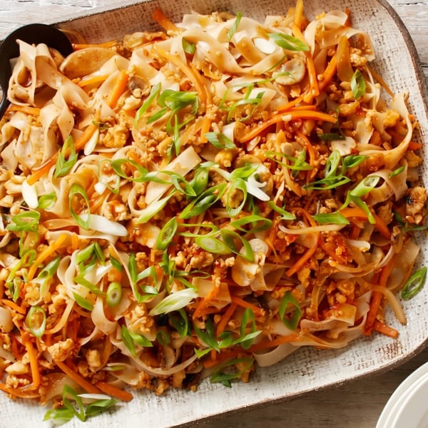 A large platter of Pad See Ew noodles with chicken, carrots, mushrooms, and green onions.