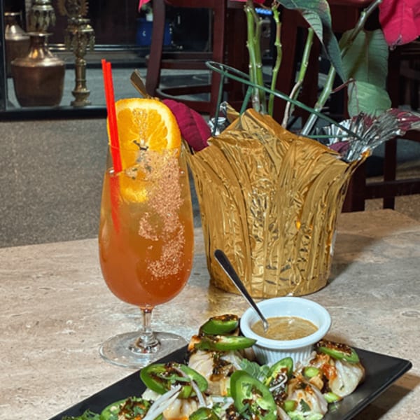 Dumplings topped with jalapeños and sauce, a cocktail, and a poinsettia plant on a table.