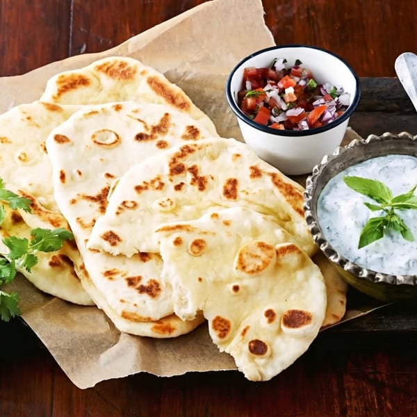 Naan bread with cilantro, salsa, and a bowl of tzatziki sauce on a wooden table.